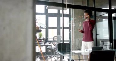 Afrika kökenli Amerikalı sıradan iş adamı ev telefonuyla konuşuyor, yavaş çekim, fotokopi alanı. İletişim, ev ofisi, uzaktan kumanda ve gelişigüzel iş, değiştirilmemiş.