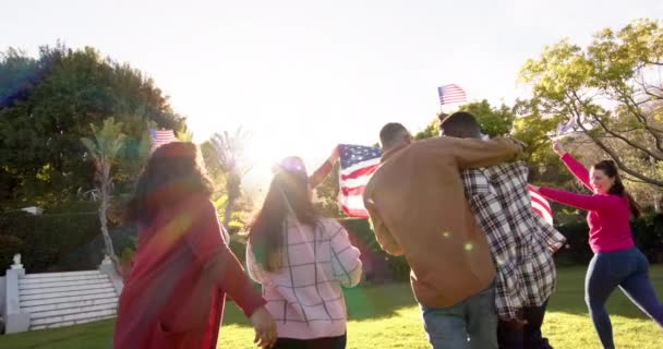 ハッピーな多様な男性と女性の友人が日当たりの良い庭で旗で踊っています 愛国心 アメリカの文化と伝統は変わらない — ストック動画