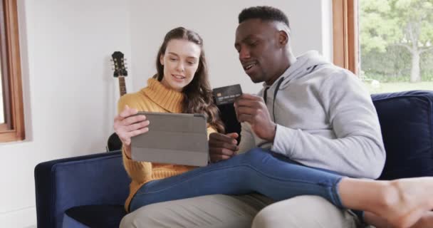 Щаслива Різноманітна Пара Сидить Дивані Використовуючи Планшет Кредитну Картку Вдома — стокове відео