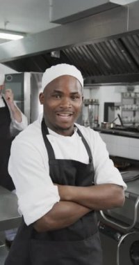 Mutlu Afro-Amerikan erkek aşçı mutfakta kolları çapraz duruyor, ağır çekimde, dikey. Aşçılık, meslek, yemek, restoran ve catering, değiştirilmemiş.