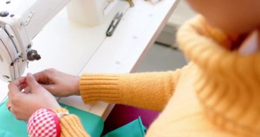 Çift ırklı kadın moda tasarımcısı dikiş makinesi stüdyoda, ağır çekimde. Moda, tasarım, giysi, perakende ve yaratıcı iş, değiştirilmemiş.