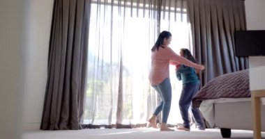 Mutlu çift ırklı anne ve kız dansları ve güneşli yatak odasında kucaklaşmalar. Aile, annelik, refah, çocukluk ve beraberlik, değişmemiş..