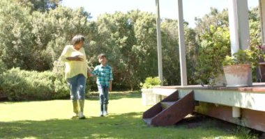 Mutlu çift ırklı büyükanne ve torun güneşli bahçede yürüyor, yavaş çekim, kopyalama alanı. Aile, birliktelik, doğa ve yaşam tarzı, değişmemiş..