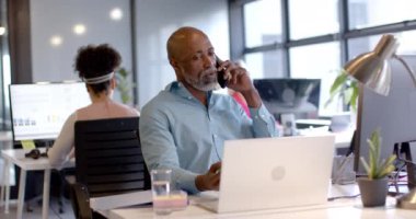 Afrika kökenli Amerikalı iş adamı ofiste akıllı telefon ve laptop kullanıyor. İş, iş, ofis, teknoloji ve takım çalışması konsepti, değiştirilmemiş.