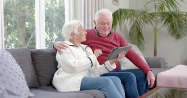 Mutlu Kafkasyalı çift koltukta oturup tablet kullanıyor, ağır çekimde. Kıdemli yaşam tarzı, iletişim ve aile hayatı, değişmeden..
