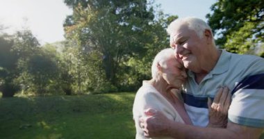 Güneşli bahçede kucaklaşan, yavaş çekimde fotokopi çeken mutlu Kafkasyalı çift. Kıdemli yaşam tarzı, birliktelik, yaz ve doğa, değişmez..