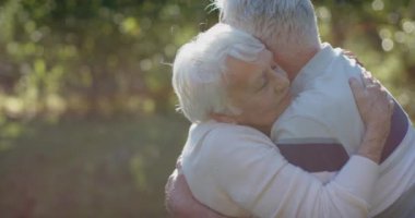 Güneşli bahçede kucaklaşan, yavaş çekimde fotokopi çeken mutlu Kafkasyalı çift. Kıdemli yaşam tarzı, birliktelik, yaz ve doğa, değişmez..