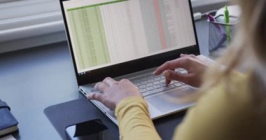 Evde dizüstü bilgisayar kullanan melez bir kadının orta kısmı, ağır çekimde. Uzaktan çalışma, iş, iletişim, yaşam tarzı ve ev hayatı.