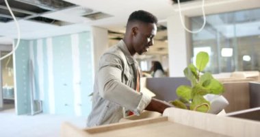 Sıradan bir Afrikalı Amerikalı iş adamı ofise kutu taşıyor, fotokopi alanı ile ağır çekimde. Günlük iş, iş, ofis ve bağlantı konsepti, değiştirilmemiş.