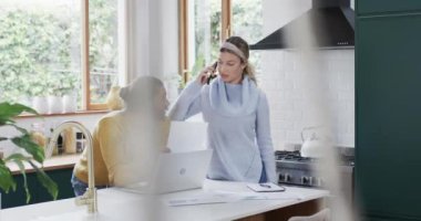 Evdeki mutfakta dizüstü bilgisayarı ve akıllı telefonu yavaş çekimde kullanan bir çift. İlişki, birliktelik, iletişim, yaşam tarzı ve aile hayatı, değişmedi..