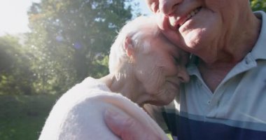 Güneşli bahçede sarılıp öpüşen Kafkasyalı mutlu çift, yavaş çekim. Kıdemli yaşam tarzı, birliktelik, yaz ve doğa, değişmez..