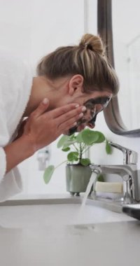 Banyoda güzellik maskesi yıkayan melez bir kadının dikey videosu, yavaş çekim. Kişisel bakım, yaşam tarzı ve ev hayatı, değişmedi..