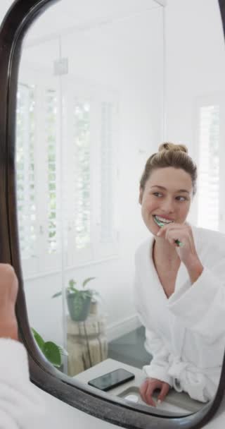 トイレで鏡を見ながら歯を磨く女性の垂直ビデオ ゆっくりとした動き セルフケア ライフスタイル 家庭生活 変わらない — ストック動画