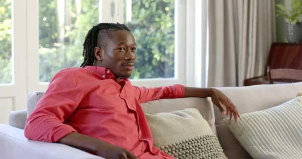 一个快乐的非洲裔美国人的画像 他在阳光充足的房间里 坐在沙发上 面带笑容 动作缓慢 家庭生活和生活方式 — 图库视频影像