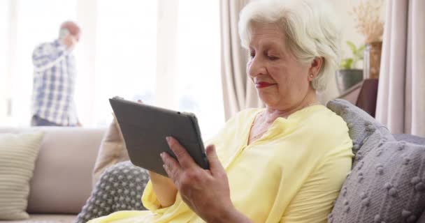 快乐多样的老夫妇使用智能手机和平板电脑在阳光灿烂的客厅里 慢动作 家庭生活和老年生活方式 — 图库视频影像