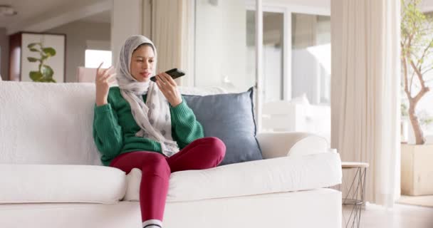 Mulher Biracial Hijab Usando Smartphone Sofá Casa Com Espaço Cópia — Vídeo de Stock