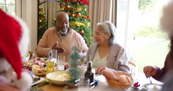 友人とクリスマスディナーテーブルで話すハッピーな多様なシニアカップル スローモーション クリスマス お祝い そしてシニアライフスタイル 変わらない — ストック動画