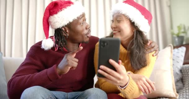 Feliz Pareja Diversa Sombreros Navidad Con Teléfono Inteligente Hablando Sofá — Vídeo de stock