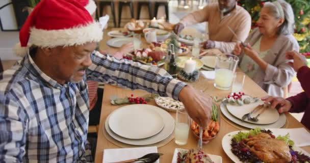 クリスマスのディナーテーブルで食べ物を提供する多様なシニア男性と女性の友人 スローモーション クリスマス お祝い そしてシニアライフスタイル 変わらない — ストック動画