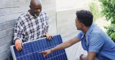 Afrikalı Amerikalı baba güneşli bahçede güneş panelini yetişkin oğluna gösteriyor, yavaş çekim. Güneş enerjisi, fotovoltaik panel, öğrenme, birliktelik, babalık, aile ve yaşam tarzı, değişmemiş..