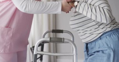 Kafkas kadın hemşire ve yürüyen çerçeveli, fotokopi alanı, ağır çekimde kıdemli Afrikalı Amerikalı kadın. Yaşlılar yaşam tarzı, hemşire, sağlık, bakım, ilaç, meslek, iş kavramı, değiştirilmemiş.