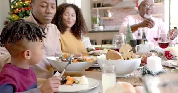 ハッピーアフリカ系アメリカ人の父親は 家族のクリスマスディナーテーブルで息子の食べ物を提供しています クリスマス お祝い トータルネスと家庭生活 変わらない — ストック動画