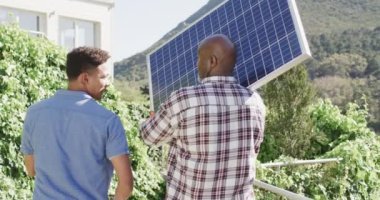 Afrika kökenli Amerikalı baba elinde güneş paneli tutarak güneşli bahçede oğluyla konuşuyor, ağır çekimde. Güneş enerjisi, fotovoltaik panel, öğrenme, birliktelik, babalık, aile ve yaşam tarzı, değişmemiş..
