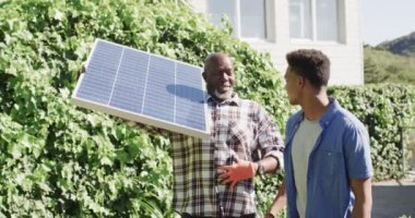 Güneş paneli olan mutlu Afro-Amerikan babası güneşli bahçede oğluyla konuşuyor, ağır çekimde. Güneş enerjisi, fotovoltaik panel, öğrenme, birliktelik, babalık, aile ve yaşam tarzı, değişmemiş..