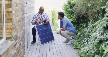 Afrikalı Amerikalı baba güneşli bahçede güneş panelini yetişkin oğluna gösteriyor. Kopya alanı, ağır çekim. Güneş enerjisi, fotovoltaik panel, öğrenme, birliktelik, babalık, aile ve yaşam tarzı, değişmemiş..