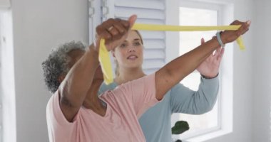 Kafkas hemşire ve yaşlı kadın lastik bantla egzersiz yapıyorlar, kopyalama alanı, yavaş çekim. Yaşlılar yaşam tarzı, hemşire, sağlık hizmetleri, bakım, tıp, meslek, iş kavramı, değiştirilmemiş.