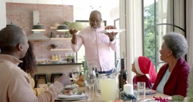 Mutlu Afro-Amerikan büyükbabası Noel yemeği masasında oturan aileye bulaşık servisi yapıyor. Noel, kutlama, aile, gelenek, birliktelik ve aile hayatı değişmedi..