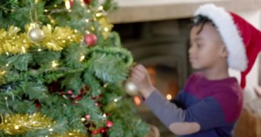 Noel şapkalı mutlu Afrikalı Amerikalı çocuk Noel ağacını süslüyor, ağır çekimde. Çocukluk, Noel, kutlama, gelenek ve aile hayatı, değişmeden.