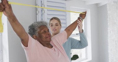 Kafkas hemşire ve yaşlı kadın lastik bantla egzersiz yapıyorlar, kopyalama alanı, yavaş çekim. Yaşlılar yaşam tarzı, hemşire, sağlık hizmetleri, bakım, tıp, meslek, iş kavramı, değiştirilmemiş.