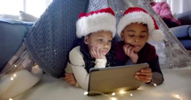 Afrika kökenli Amerikalı erkek ve kız kardeşler noel şapkalarında battaniye çadırında tablet kullanıyorlar, ağır çekimde. İletişim, çocukluk, Noel, kutlama, aile, birliktelik ve aile hayatı, değişmemiş.