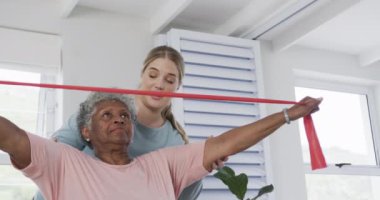 Kafkas hemşire ve yaşlı kadın lastik bantla egzersiz yapıyorlar, kopyalama alanı, yavaş çekim. Yaşlılar yaşam tarzı, hemşire, sağlık hizmetleri, bakım, tıp, meslek, iş kavramı, değiştirilmemiş.