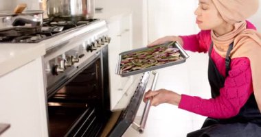 Türbanlı kadın evdeki mutfak tepsisini fotokopi odasıyla fırına koyuyor, ağır çekimde. Yaşam tarzı, ev hayatı, yemek, yemek hazırlama konsepti, değiştirilmemiş.