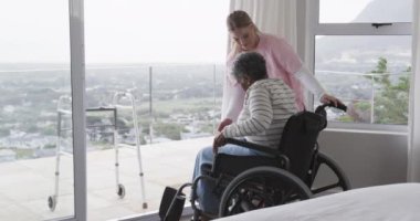 Yaşlı Afrikalı Amerikalı kadın hasta tekerlekli sandalyede ağır çekimde gülümseyen beyaz hemşire. Yaşlılar yaşam tarzı, hemşire, sağlık hizmetleri, bakım, tıp, meslek, iş kavramı, değiştirilmemiş.