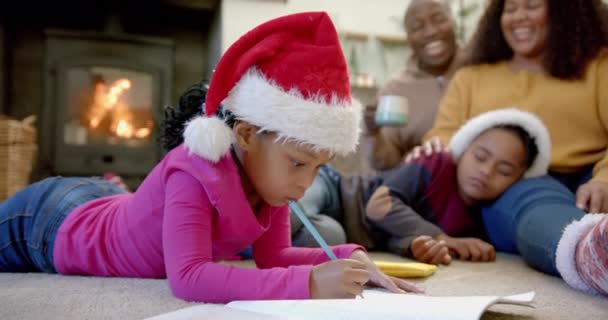 クリスマスの帽子をかぶったハッピーアフリカ系アメリカ人の娘は 両親と一緒に眠り ゆっくりとした動き クリエイティビティ 子供時代 クリスマス お祝い 家族とトグルネス 変わらない — ストック動画