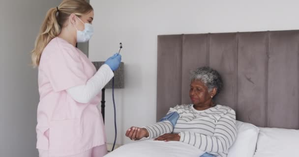 Белая Медсестра Маске Проверяет Давление Пожилой Африканской Женщины Замедленная Съемка — стоковое видео