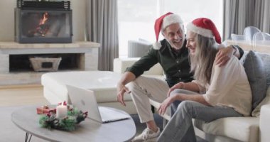Evde Noel Baba şapkalı orta yaşlı beyaz bir çift Noel Baba 'nın bilgisayarında görüntülü sohbet ediyor. İletişim, Noel, gelenek, kutlama, yaşam tarzı ve ev hayatı, kopyalama alanı, değiştirilmemiş.