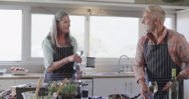 Orta yaşlı beyaz bir çift şarap içiyor, yemek hazırlıyor, mutfakta yemek pişiriyor, ağır çekimde. İlişki, yemek, yemek, yaşam tarzı ve ev hayatı, kopyalama alanı, değiştirilmemiş.