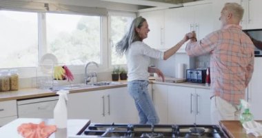 Orta yaşlı beyaz bir çift mutfakta dans ediyor, ağır çekimde. İlişki, eğlence, ev koroları, yaşam tarzı ve aile hayatı, kopyalama alanı, değiştirilmemiş.