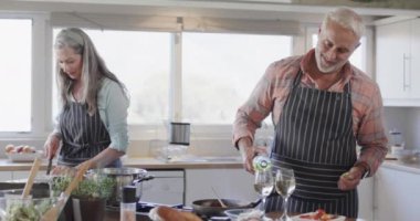 Orta yaşlı beyaz bir çift şarap dolduruyor, yemek hazırlıyor, mutfakta yemek pişiriyor, ağır çekimde. İlişki, yemek, yemek, yaşam tarzı ve ev hayatı, kopyalama alanı, değiştirilmemiş.
