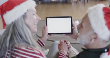 Noel 'de evde boş ekranlı tabletli orta yaşlı beyaz bir çift, ağır çekimde. İletişim, Noel, gelenek, kutlama, yaşam tarzı ve ev hayatı, kopyalama alanı, değiştirilmemiş.