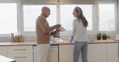 Orta yaşlı beyaz bir çift mutfakta bulaşık yıkıyor, ağır çekimde. İlişki, ev koroları, yaşam tarzı ve aile hayatı, kopya alanı, değişmemiş.