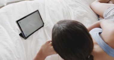 Çift ırklı bir kadın yatakta, ekranda kopya alanı olan tablet kullanıyor, yavaş çekim. Yaşam tarzı, iletişim ve aile hayatı, değişmedi..