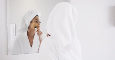 Banyoda aynaya bakarak güzellik maskesi takan mutlu, melez kadın, yavaş çekim. Yaşam tarzı, özbakım, güzellik ve ev hayatı, değişmemiş..