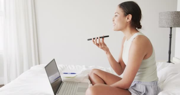 Mujer Birracial Feliz Sentado Cama Usando Ordenador Portátil Hablando Teléfono — Vídeos de Stock