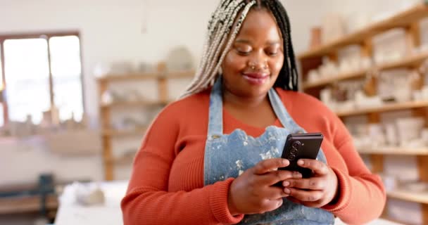 快乐的非洲裔美国女性陶工使用智能手机和微笑在陶瓷工作室 慢动作 手工制品 当地企业 业余爱好和工艺 原封不动 — 图库视频影像