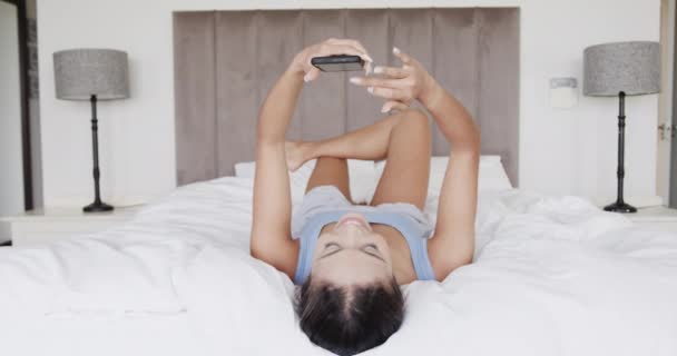Mulher Biracial Feliz Deitada Cama Usando Smartphone Câmera Lenta Estilo — Vídeo de Stock